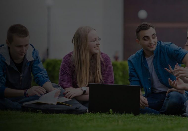 A background image for AUBG of three students sitting on the grass with laptops