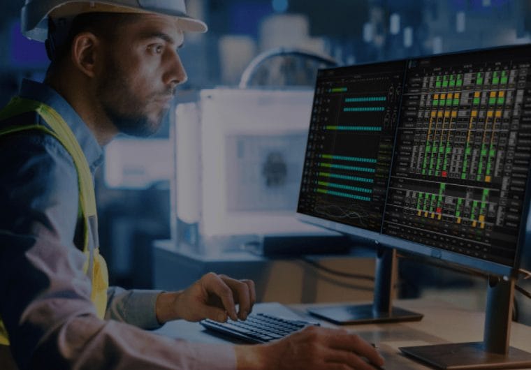 A man in a hardhat looks at graphics on a computer monitor