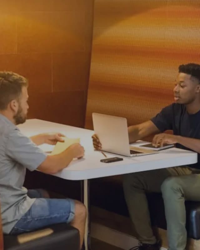 A man sitting in front of a computer and another man sitting across from him