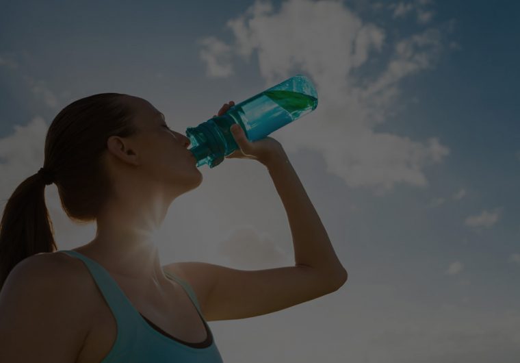 woman drinking water from a bottle with the sun and sky in the background