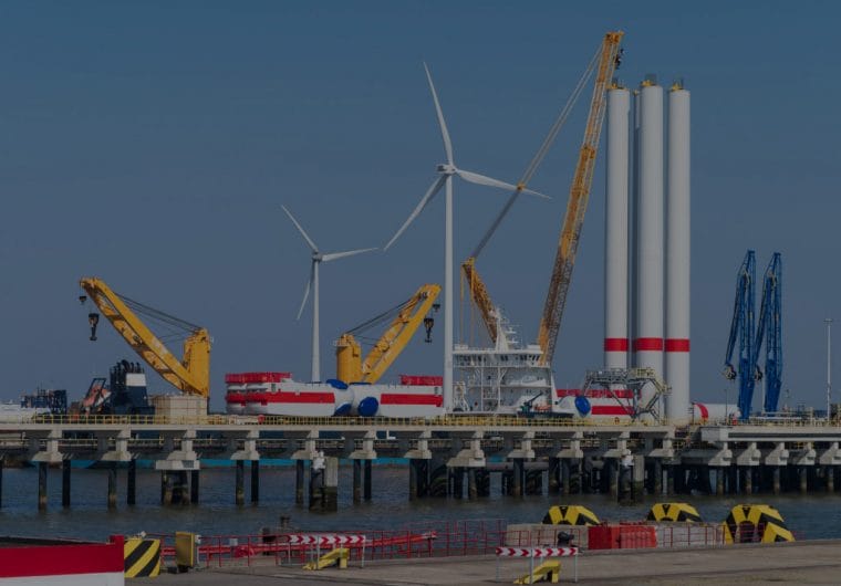 Windmills and heavy machinery are placed on a coastline and jetty