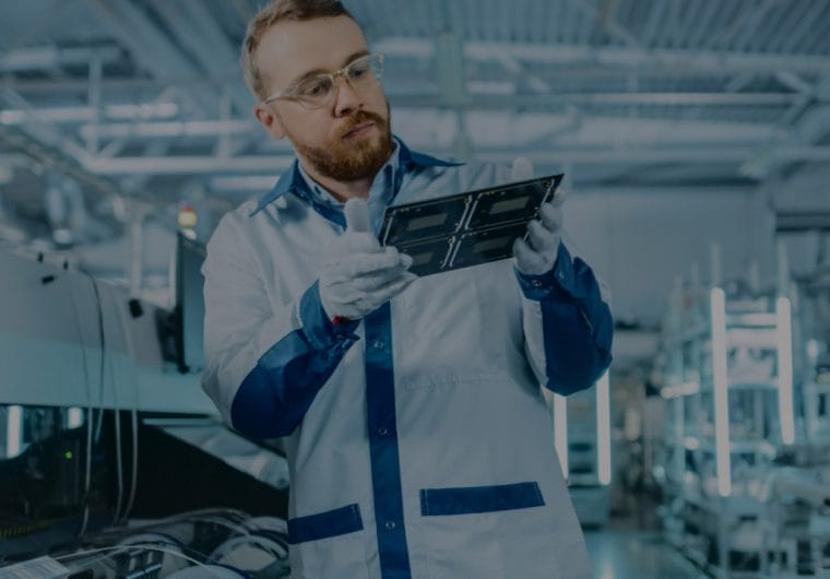 A man in a lab coat, gloves and glasses holds a sheet of material