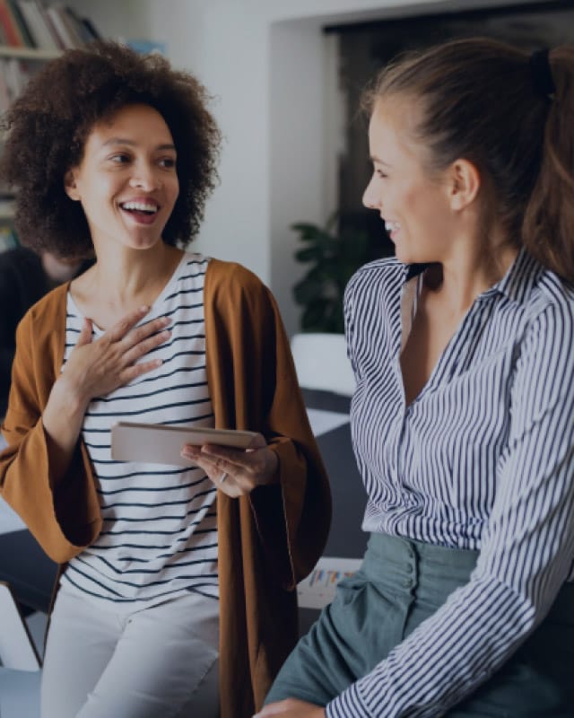 Two women laugh at each other while one holds a notepad