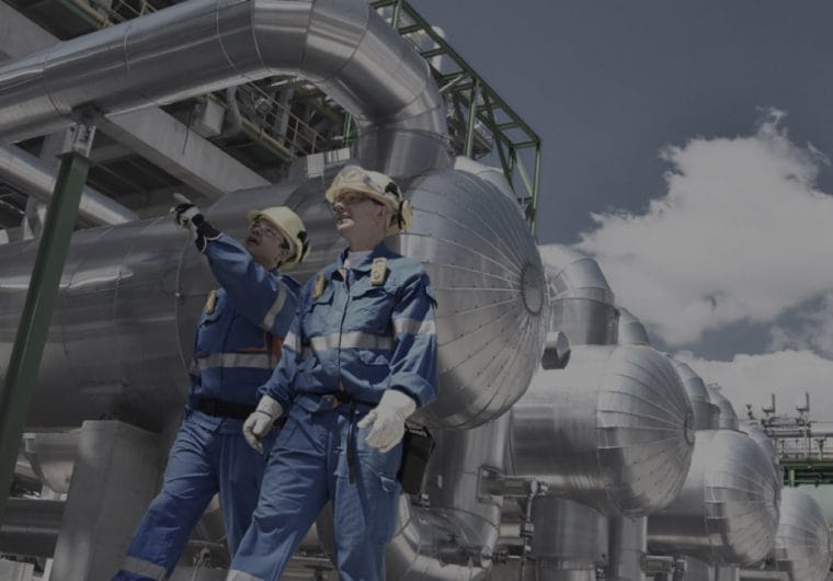 Two men in hardhats and overalls walk and point